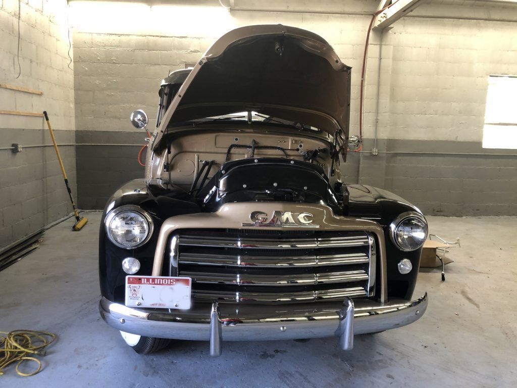 Black and tan vintage GMC truck with hood up in a garage. | Loyola Service