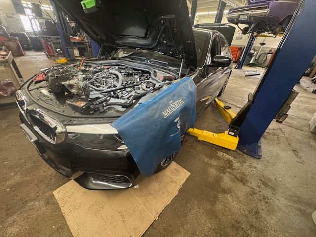 Black car with open hood, on a lift in a garage, blue fender cover in place. | Loyola Service