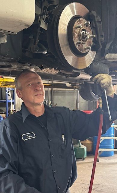 Mechanic holding tool, looking up at car brake assembly; in a garage. | Loyola Service
