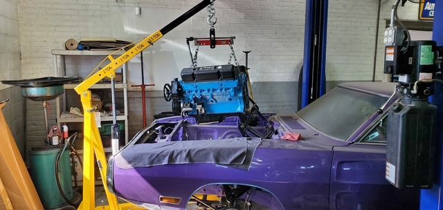 A purple car with a blue engine being lifted by a yellow engine hoist in a garage. | Loyola Service