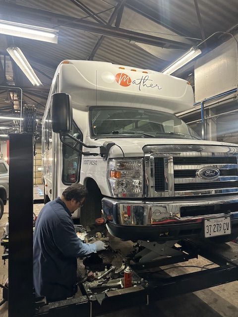 A mechanic working on the front of a white RV, inside a garage with fluorescent lights. | Loyola Service