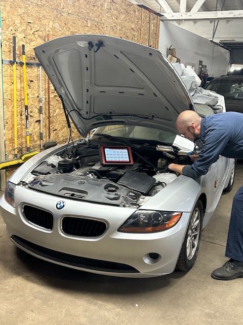 Silver BMW Z4 with hood open being inspected by a mechanic using diagnostic equipment in a garage. | Loyola Service