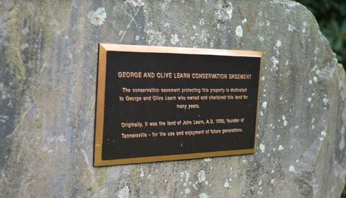 Bronze plaque on a stone, dedicated to George and Clive Leath, for conservation, in a green setting.