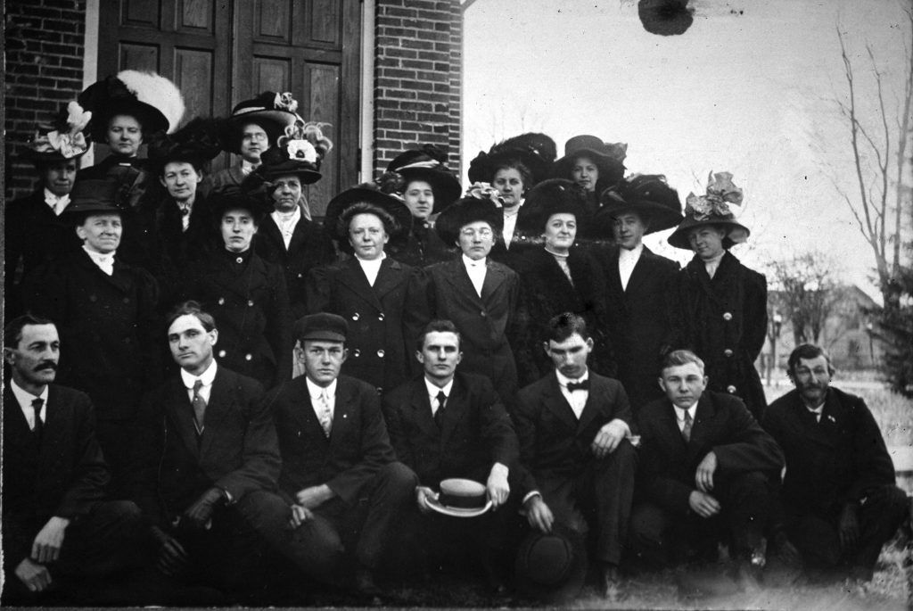 Group of men and women in dark clothing posing outside a building.