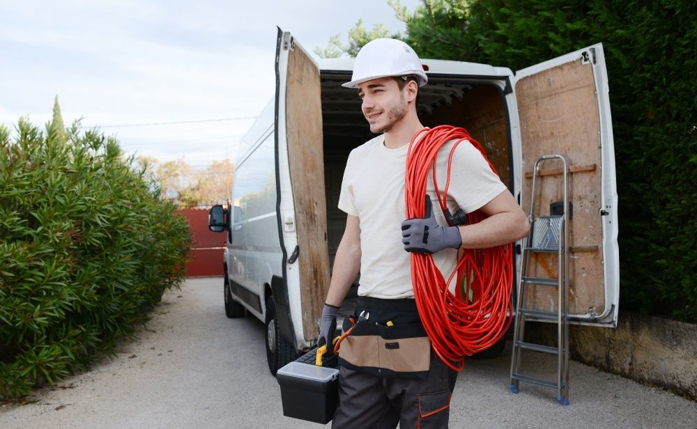 A man is carrying a hose and a toolbox in front of a van.