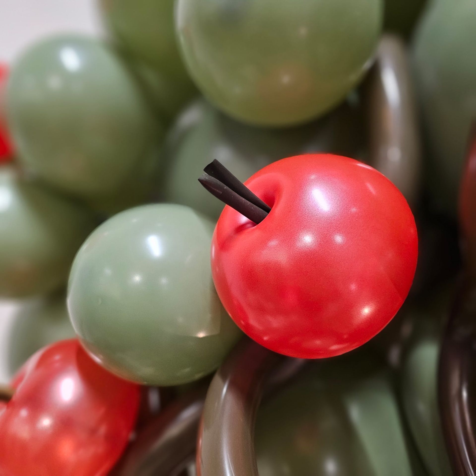 Primo piano di una composizione di palloncini rossi e verdi che ricordano le mele; bastoncini neri inseriti come steli.