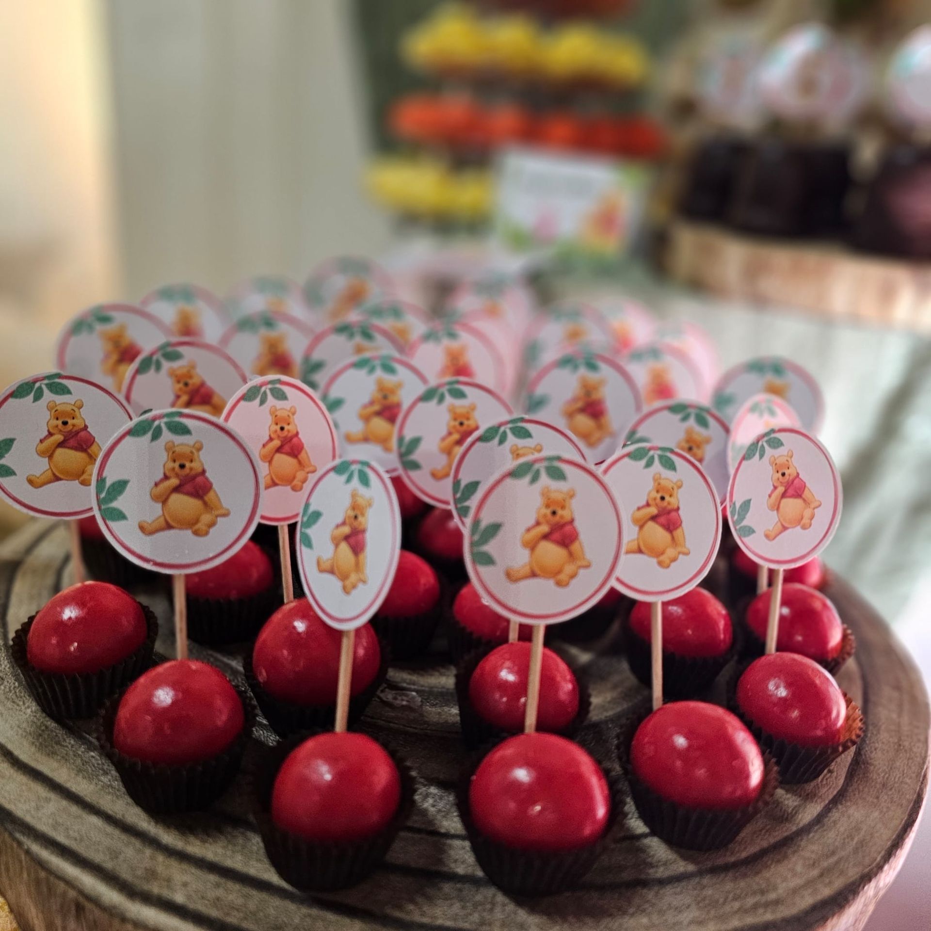 Cake pops con decorazioni di Winnie the Pooh; rivestimento rosso, su un vassoio di legno.