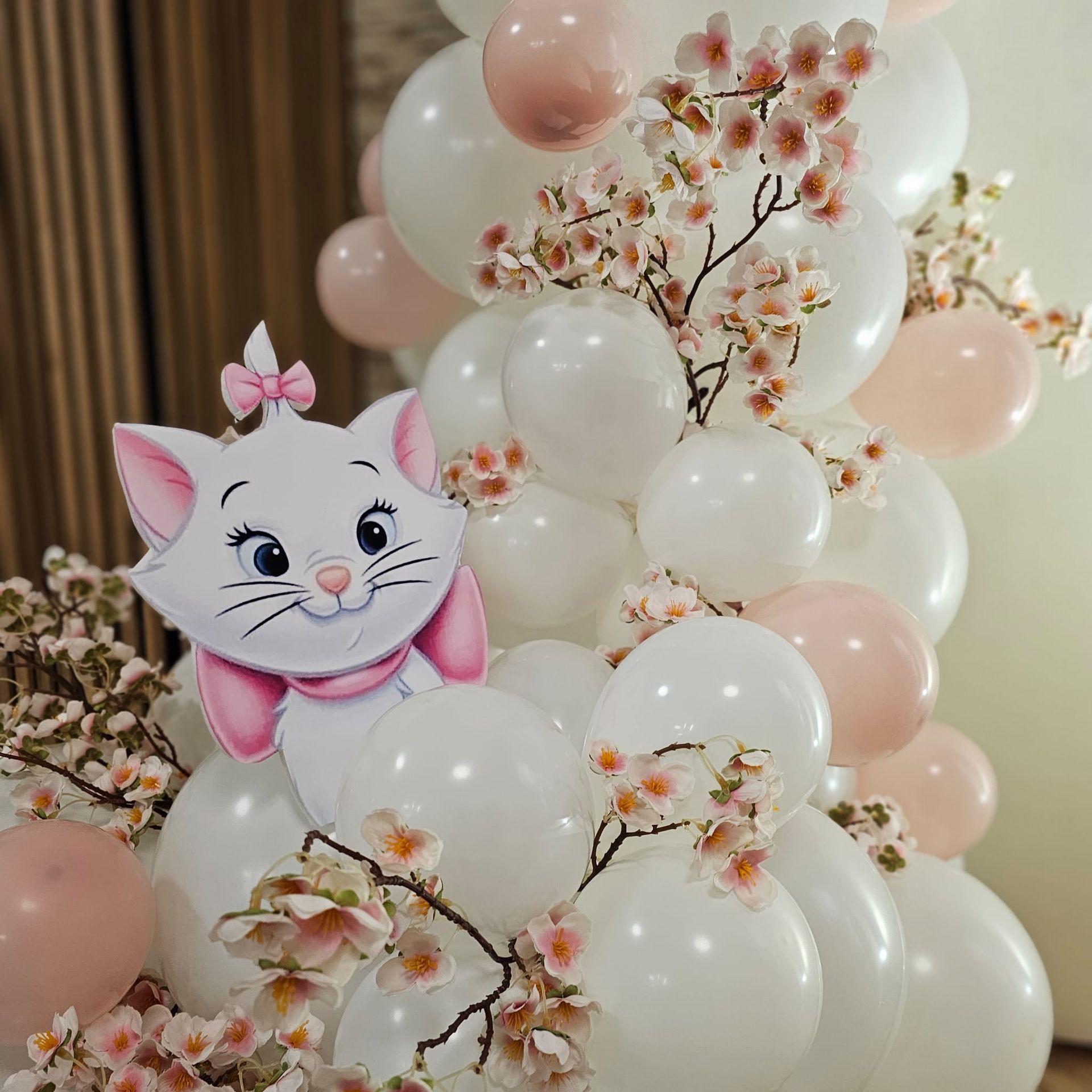 Marie l'Aristogatta circondata da palloncini bianchi e rosa, con rami di fiori.