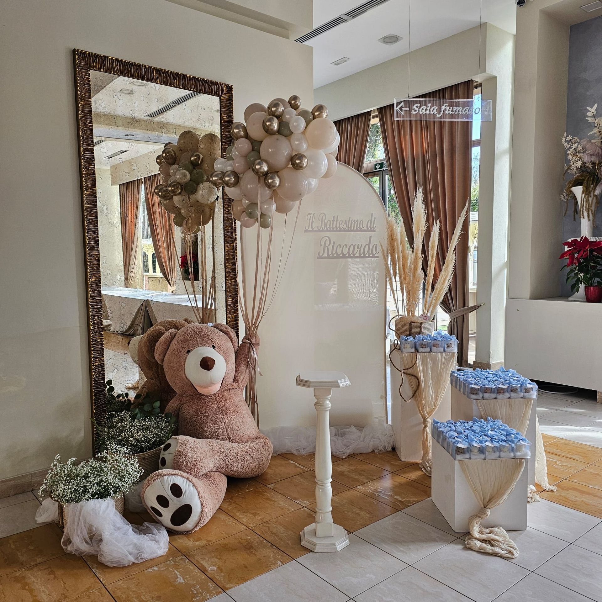 Esposizione dell'evento con orsacchiotto, palloncini, cartello e composizioni floreali.