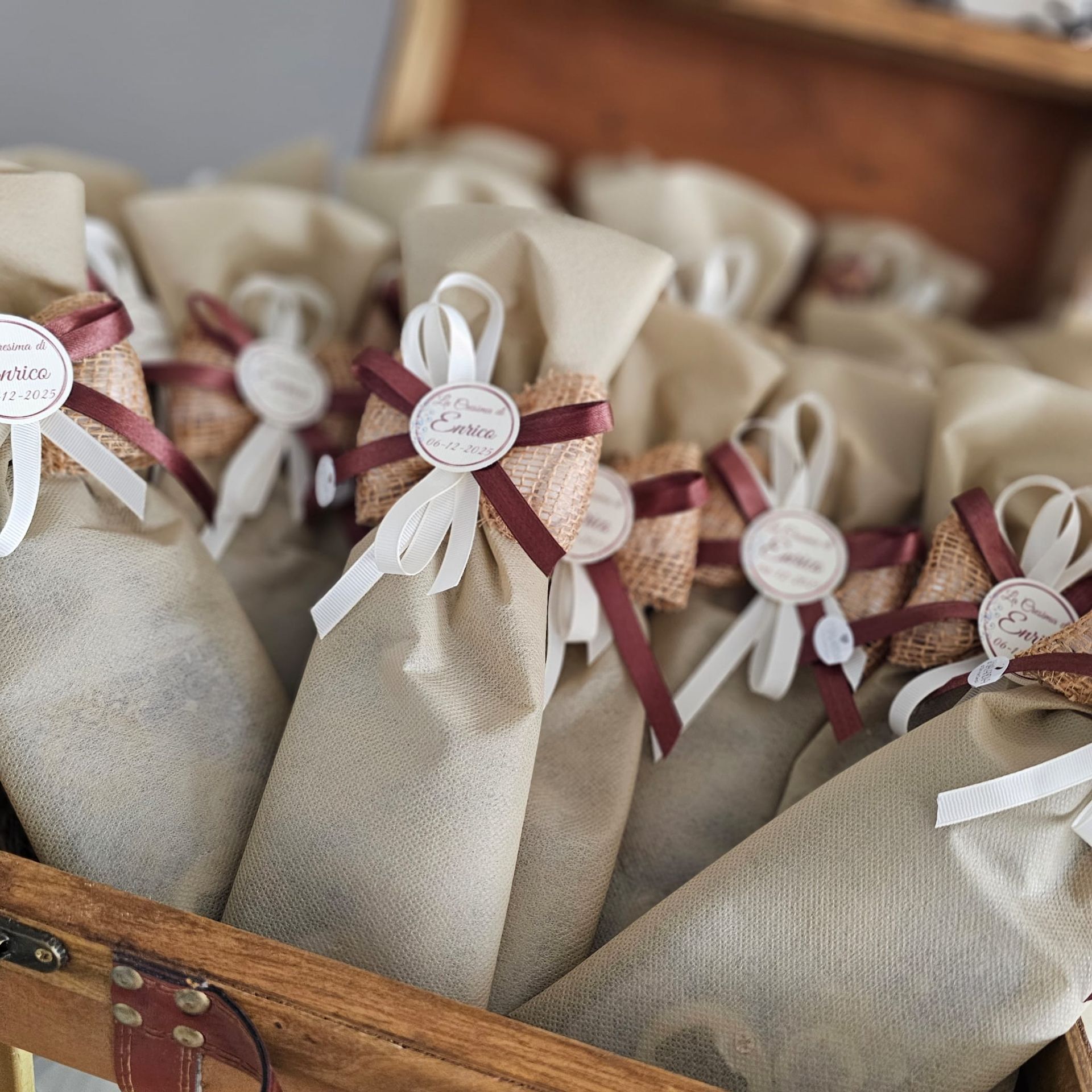 Regali avvolti in tela di iuta con nastri marroni e bianchi in una scatola di legno, probabilmente per una festa.