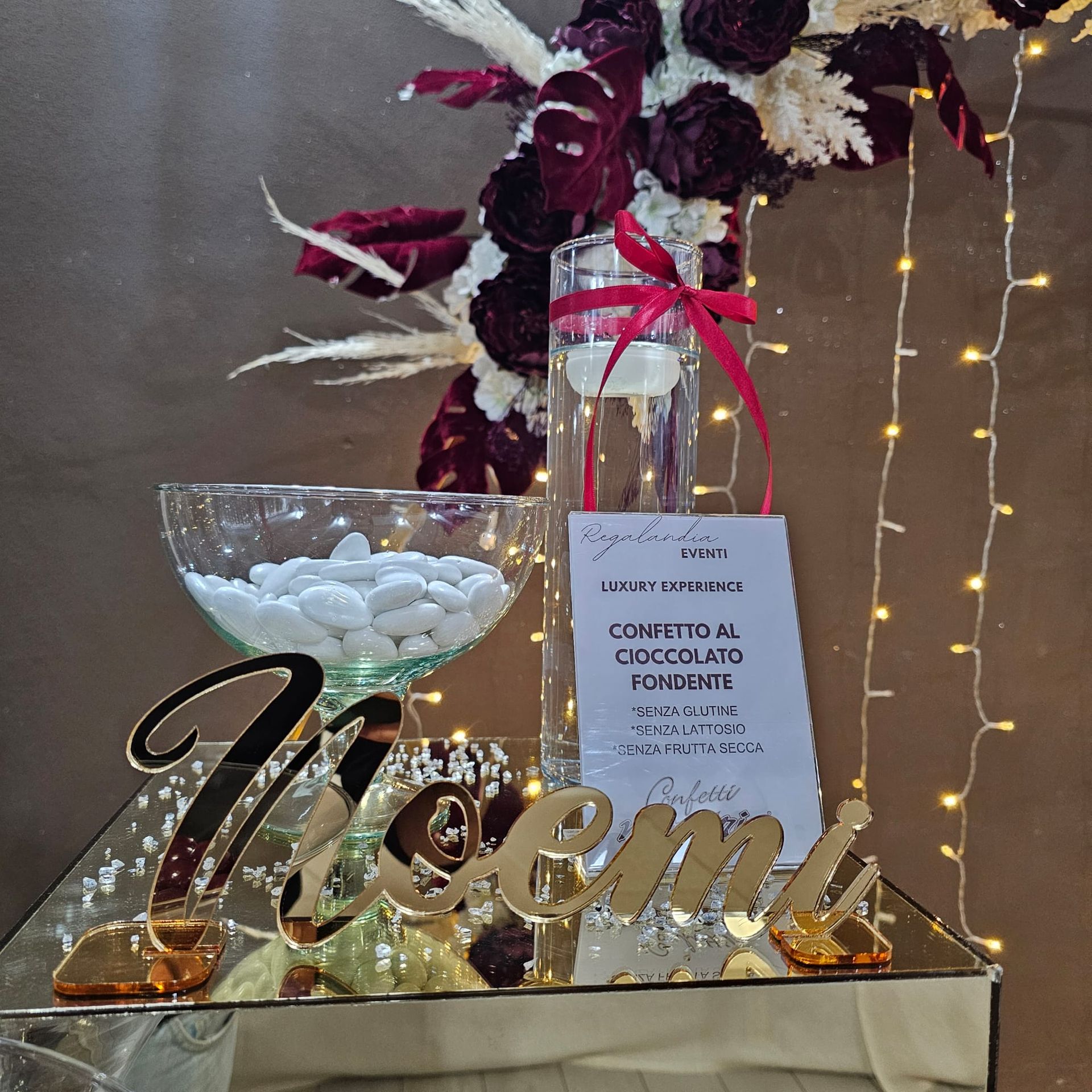 Un tavolo decorato per un evento, con dolciumi, fiori e un cartello.