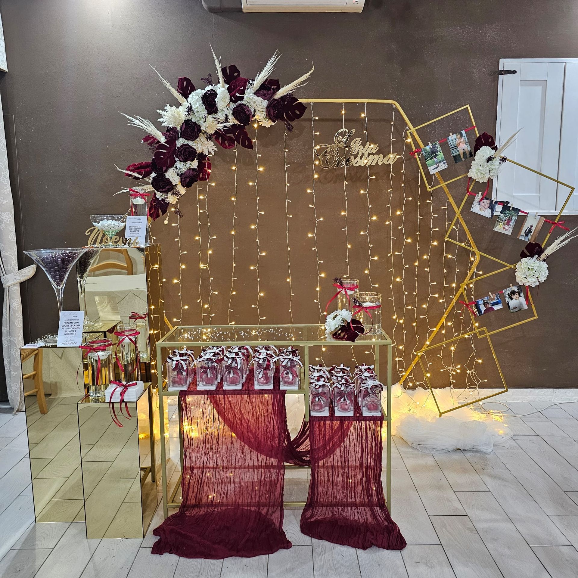 Decorazioni per il matrimonio: cornice dorata con composizione floreale, lucine, tavolo dei dolci con bomboniere e foto.