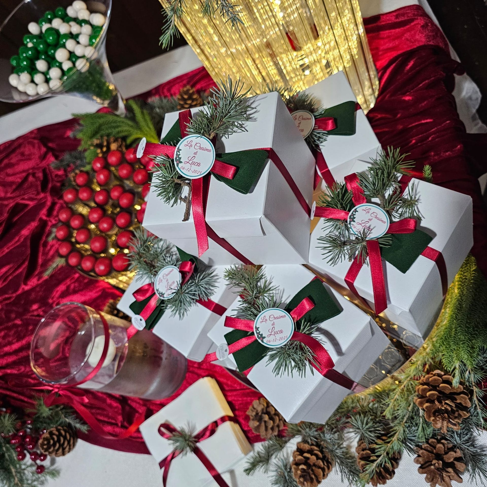 Regali di Natale: scatole bianche con nastro rosso, verde e una ghirlanda, su un panno rosso con caramelle.