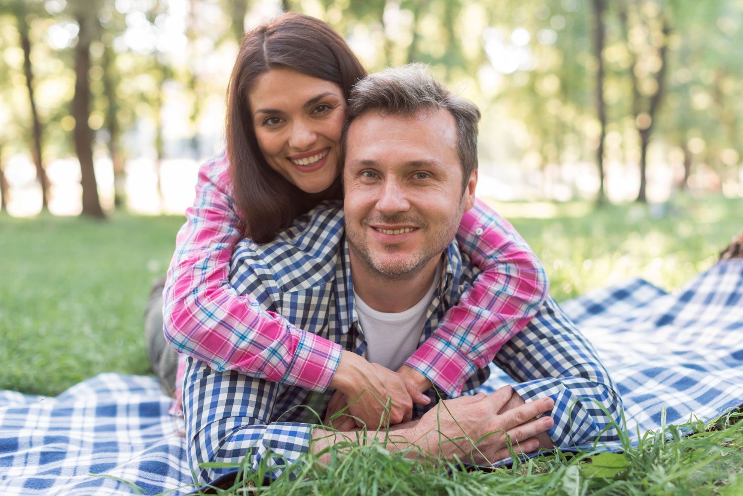 A man and a woman are laying on a blanket in the grass.