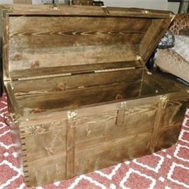 A wooden trunk with the lid open is sitting on a rug.