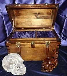 A wooden trunk is sitting on a table next to a crystal skull.