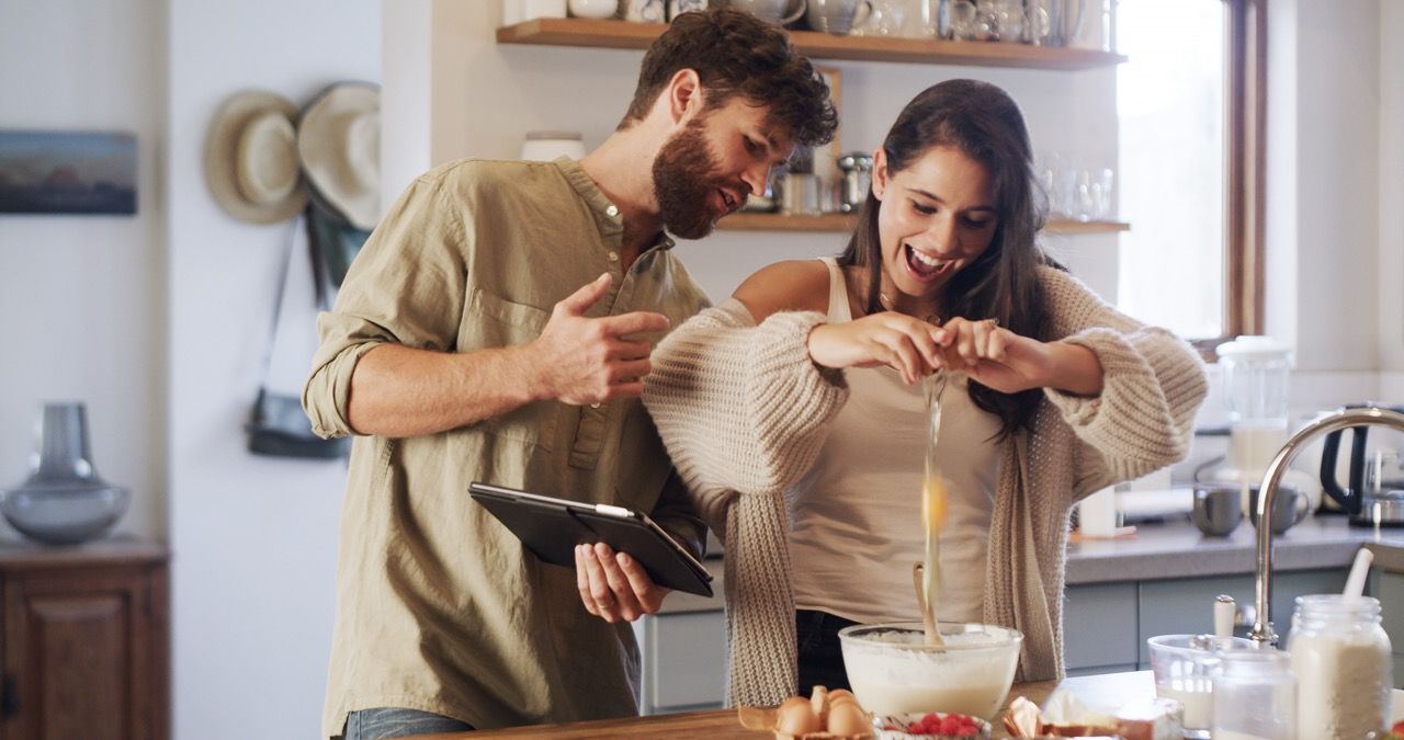 Two people in a kitchen comparing a tablet recipe while cooking together