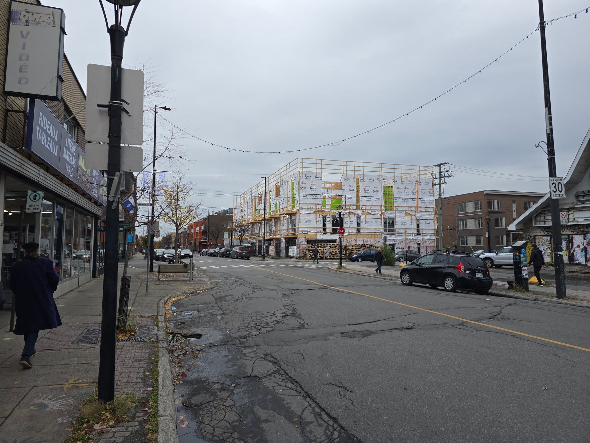 Une rue avec des voitures garées sur le côté et un bâtiment en construction en arrière-plan.