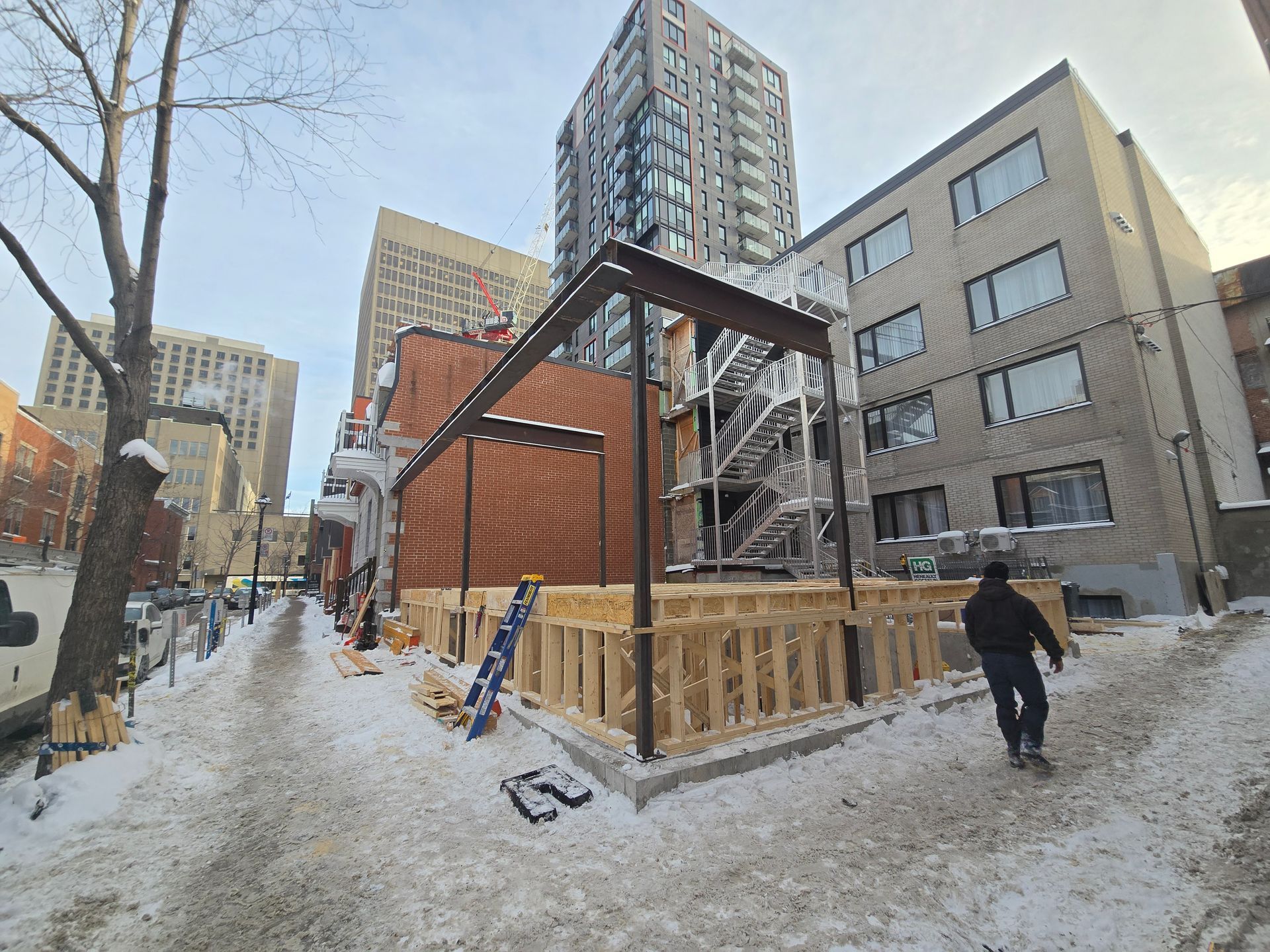 A man is walking down a snowy sidewalk in front of a building under construction.