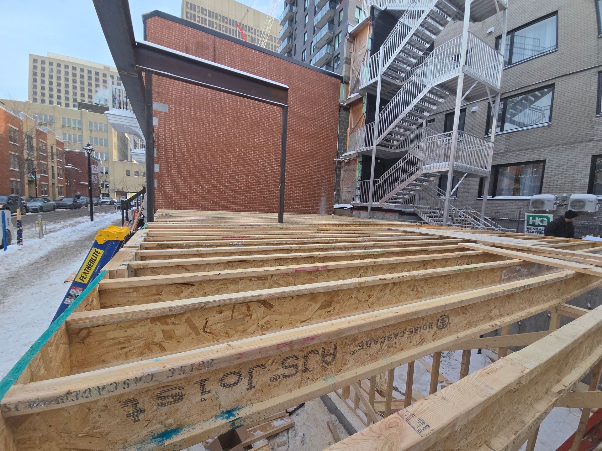 Une structure en bois est en cours de construction devant un bâtiment en briques.