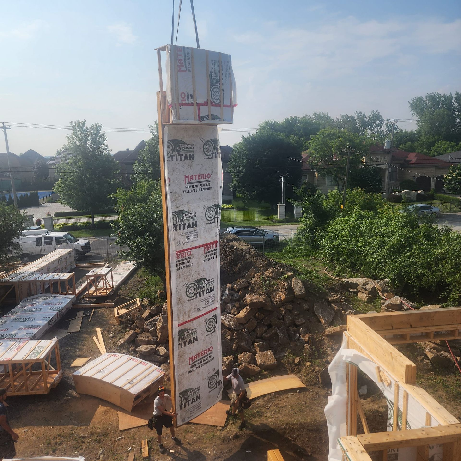 Une grue soulève un grand panneau mural lors de la construction d'un bâtiment. Deux ouvriers observent.