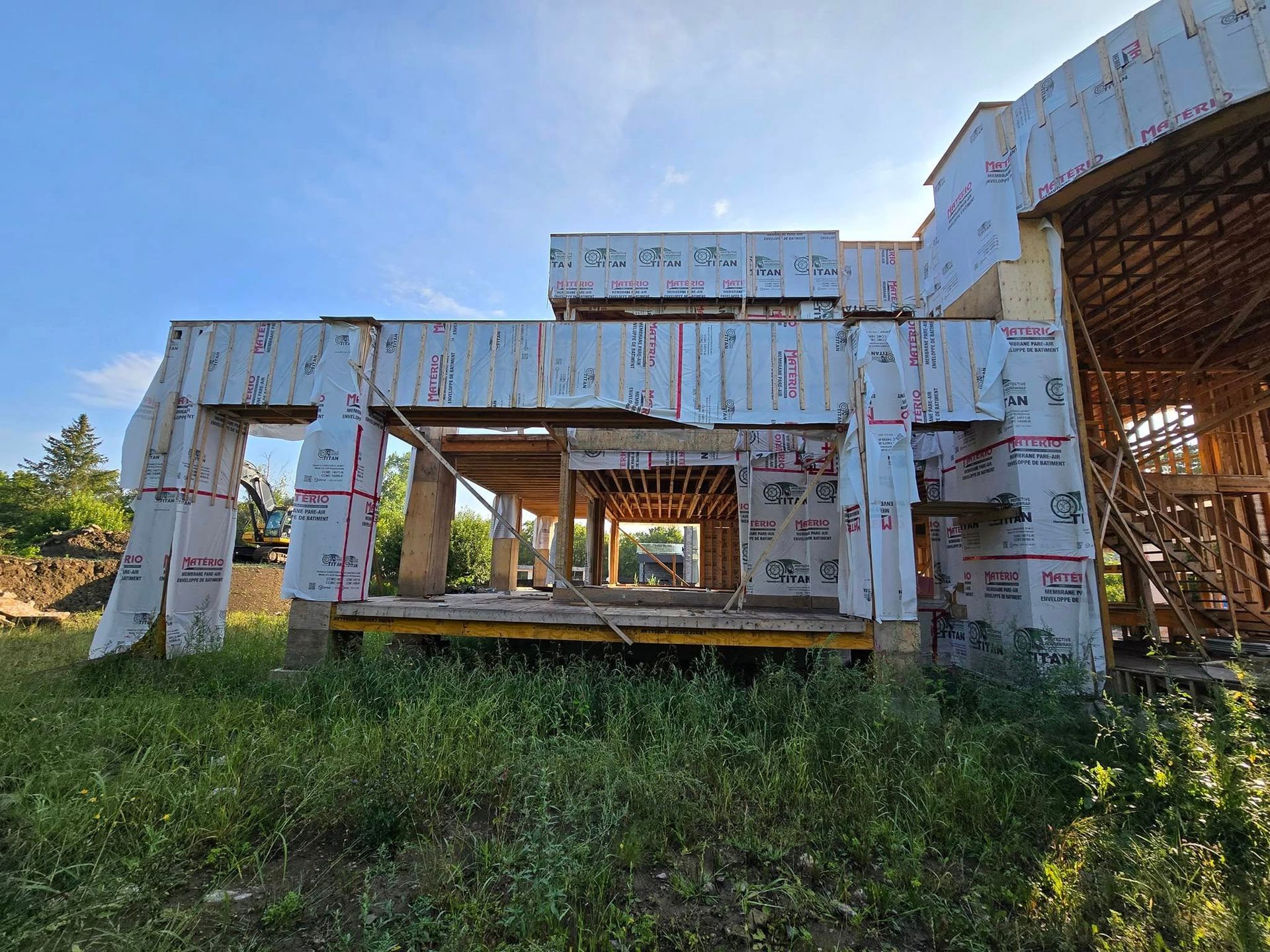 Maison en construction, ossature bois, recouverte de tissu blanc et rose. Journée ensoleillée.