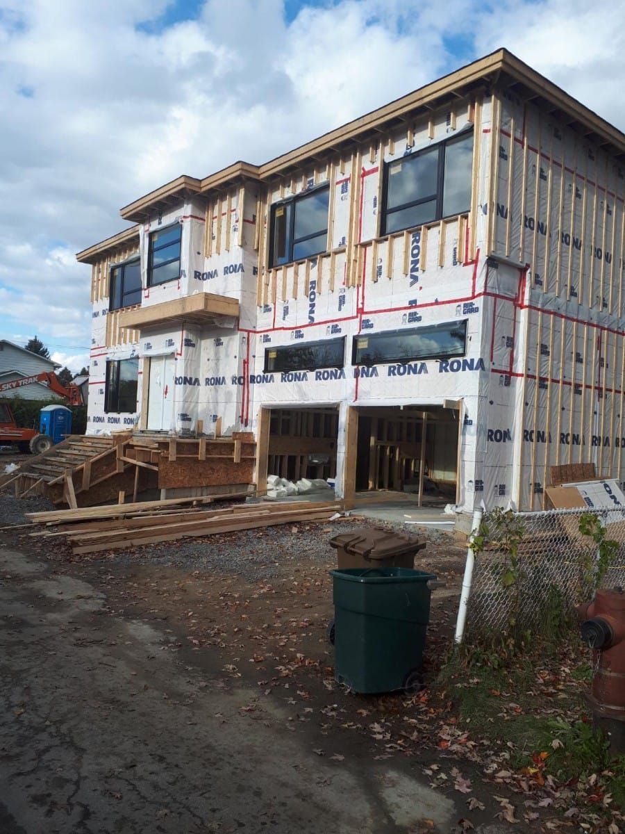 A large house under construction with a green trash can in front of it