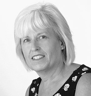 Woman with short blonde hair smiles, wearing a black and white floral print top.