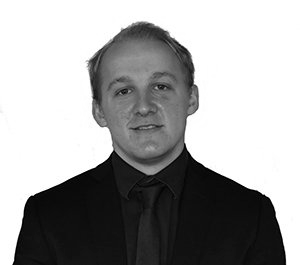 A man in a black suit and tie, looking at the camera.