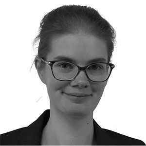 Woman with glasses smiles, wearing a dark blazer; headshot.