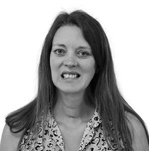 Woman with long hair, smiling with teeth, wearing a patterned blouse.