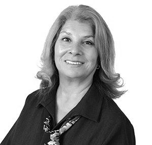 Woman with grey hair, smiling, wearing a dark shirt with floral tie.