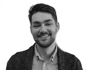 Smiling man with a beard, wearing a button-down shirt and jacket, against a white background.