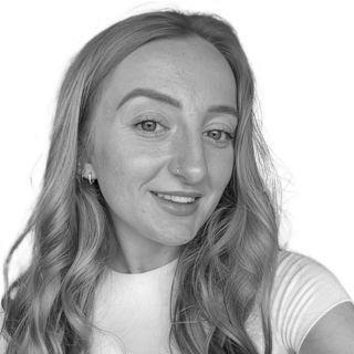 Woman with long wavy hair smiling, wearing white shirt, in front of a white background.