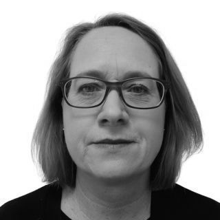 Woman with glasses, short hair, and dark clothing, looking forward. Black and white portrait.