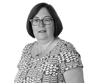 Woman with glasses, in a patterned top, looking at the camera. Black and white portrait.