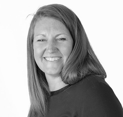 Woman with long hair smiles, looking towards the viewer in front of a white background.