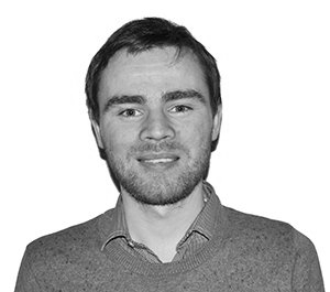 Man with light skin, short brown hair and a goatee smiling, wearing a button-down shirt and a sweater.