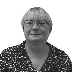 Woman with glasses smiling, wearing a patterned blouse, blonde hair, against a white background.