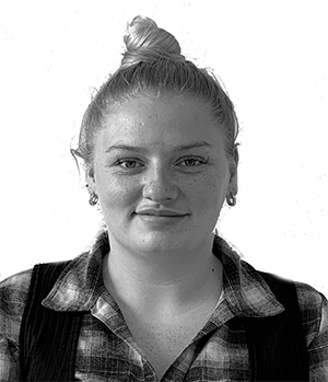 Woman with blonde hair in a bun, wearing a plaid shirt and vest, smiling at the camera.