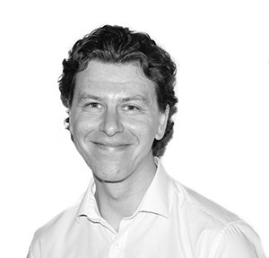 Man in a white shirt smiles at the camera. Black and white photo.