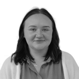 Woman with dark hair smiles, wearing a light cardigan over a button-up shirt. Studio shot.