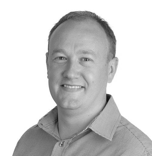 Smiling man in a light-colored collared shirt, head and shoulders portrait, against a white background.