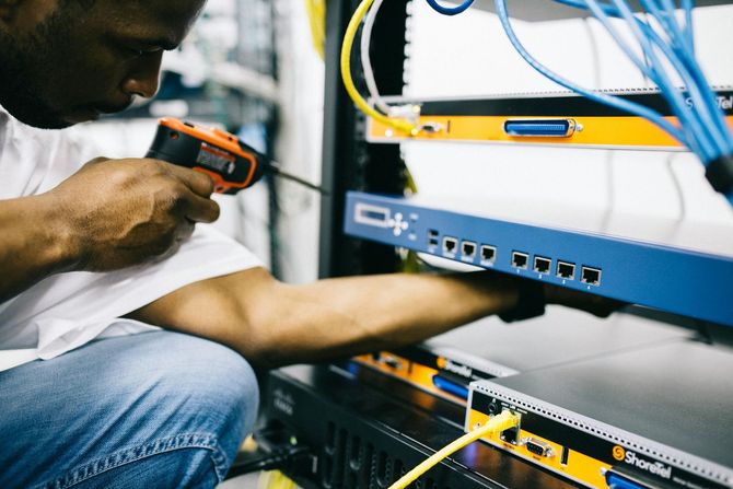 IT technician using a handheld power tool to maintain or install networking hardware in a server rack.