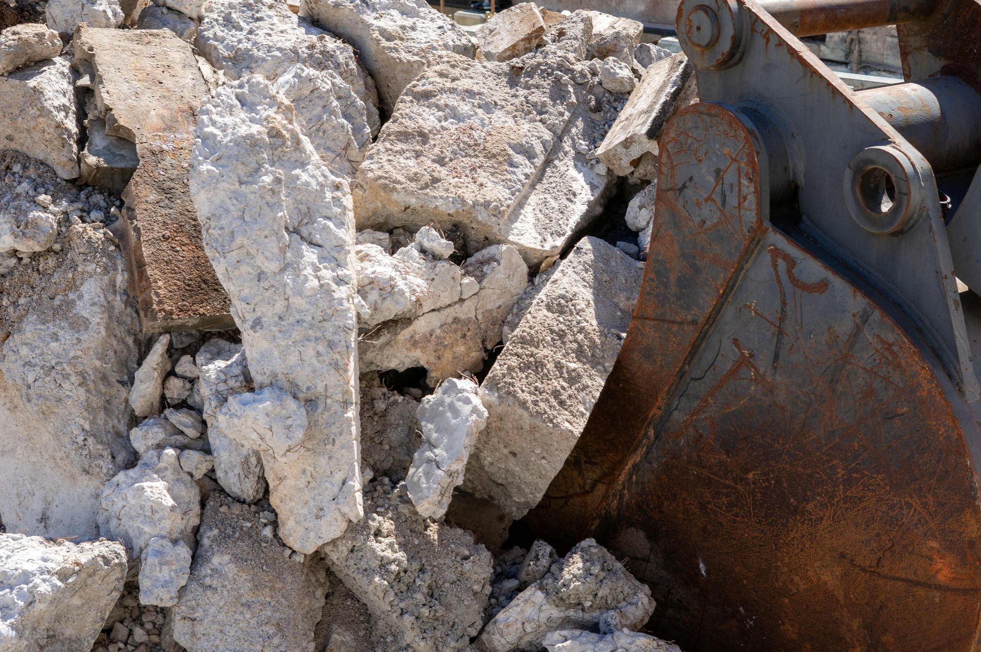 Metal excavator bucket with large concrete blocks during demolition.