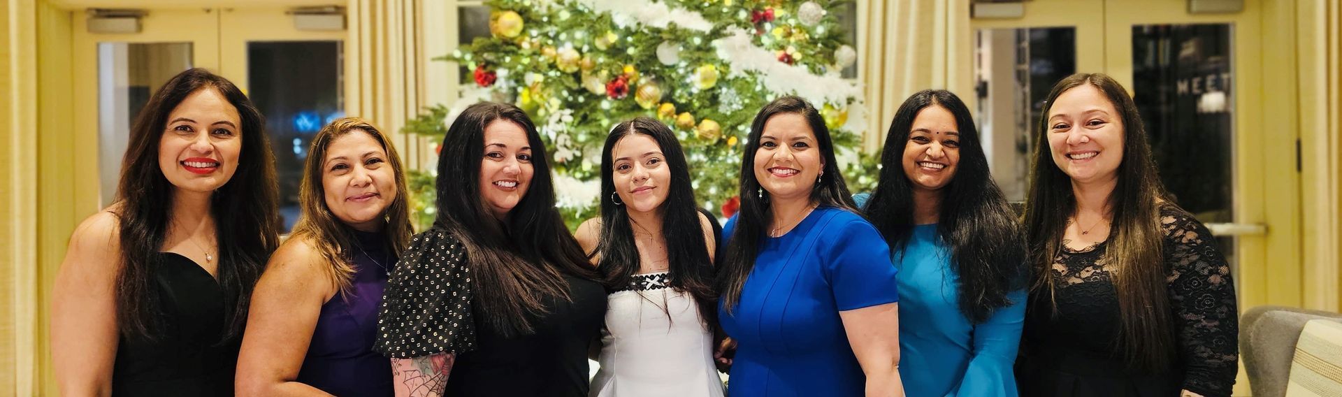 A group of women are posing for a picture in front of a christmas tree.