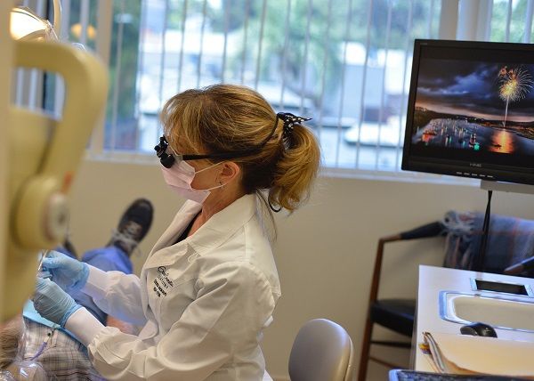 GILROY DENTAL SMILES_Dentist in mask and glasses examining patient's teeth in a dental office.