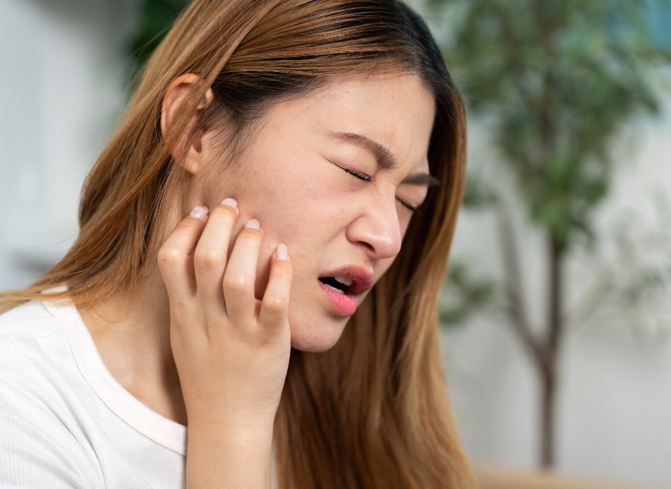 Woman with closed eyes, scratching jaw, indicating discomfort.