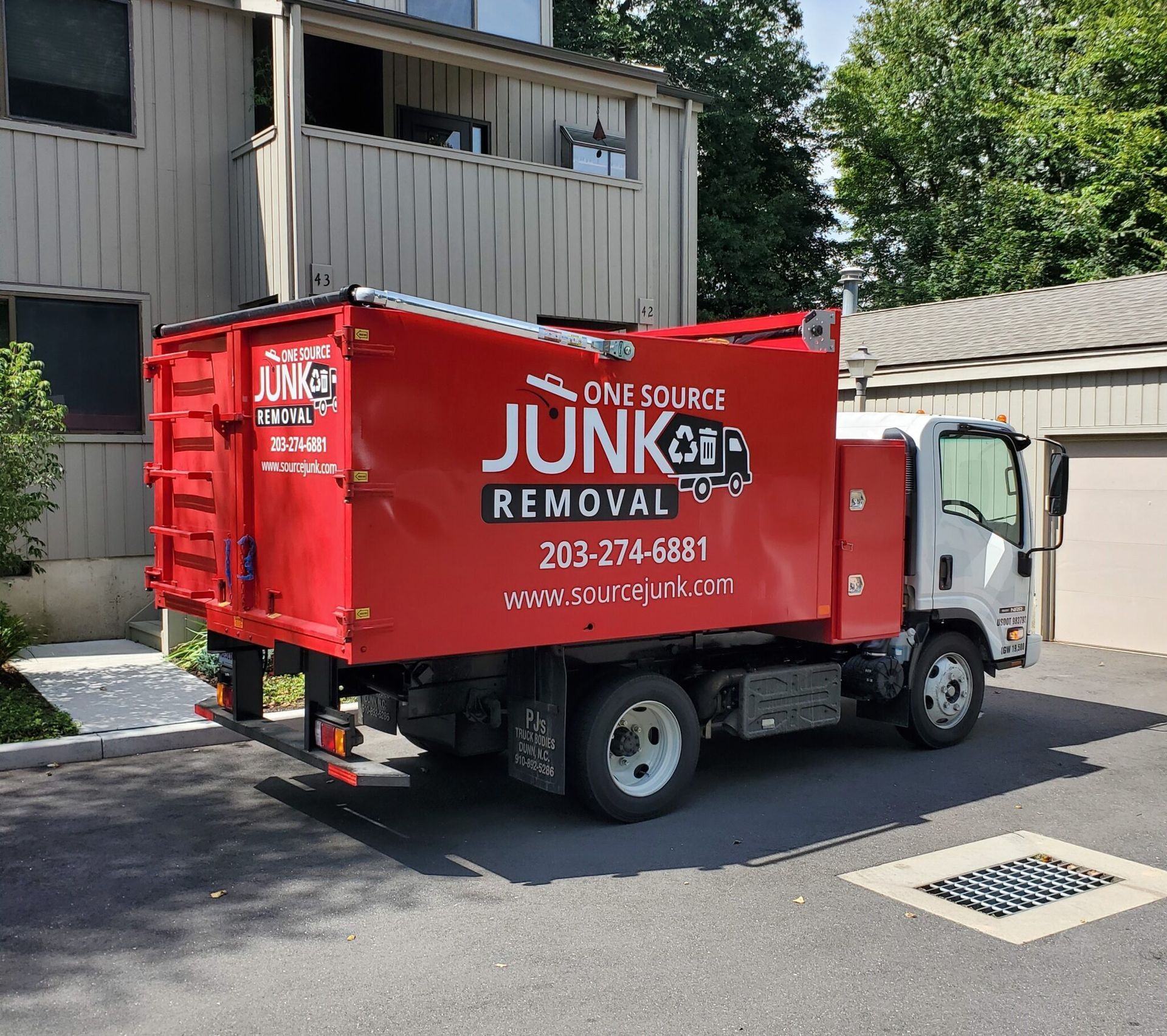 A red junk removal truck is parked in front of a building