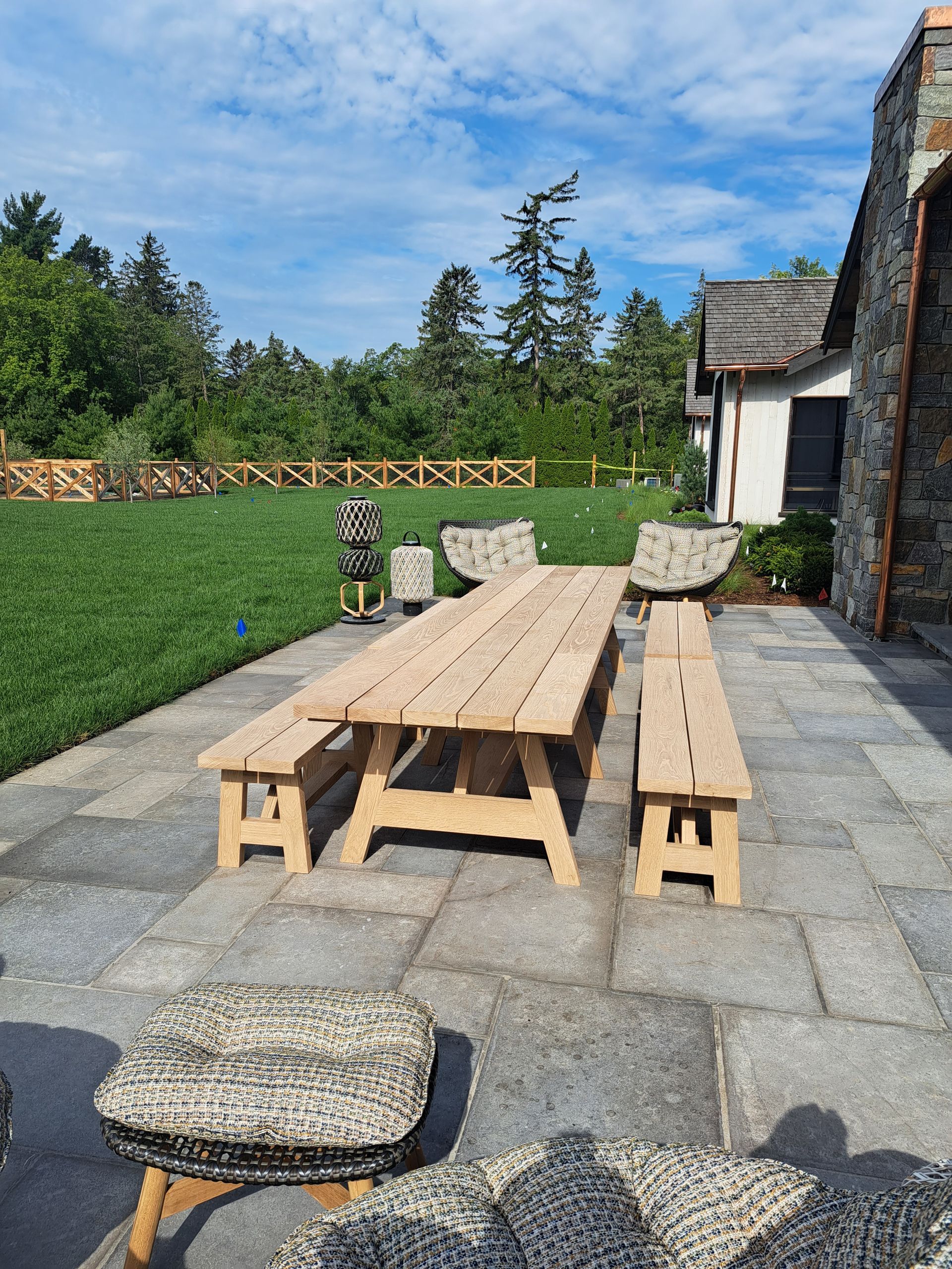 A wooden picnic table and benches on a patio in front of a house.